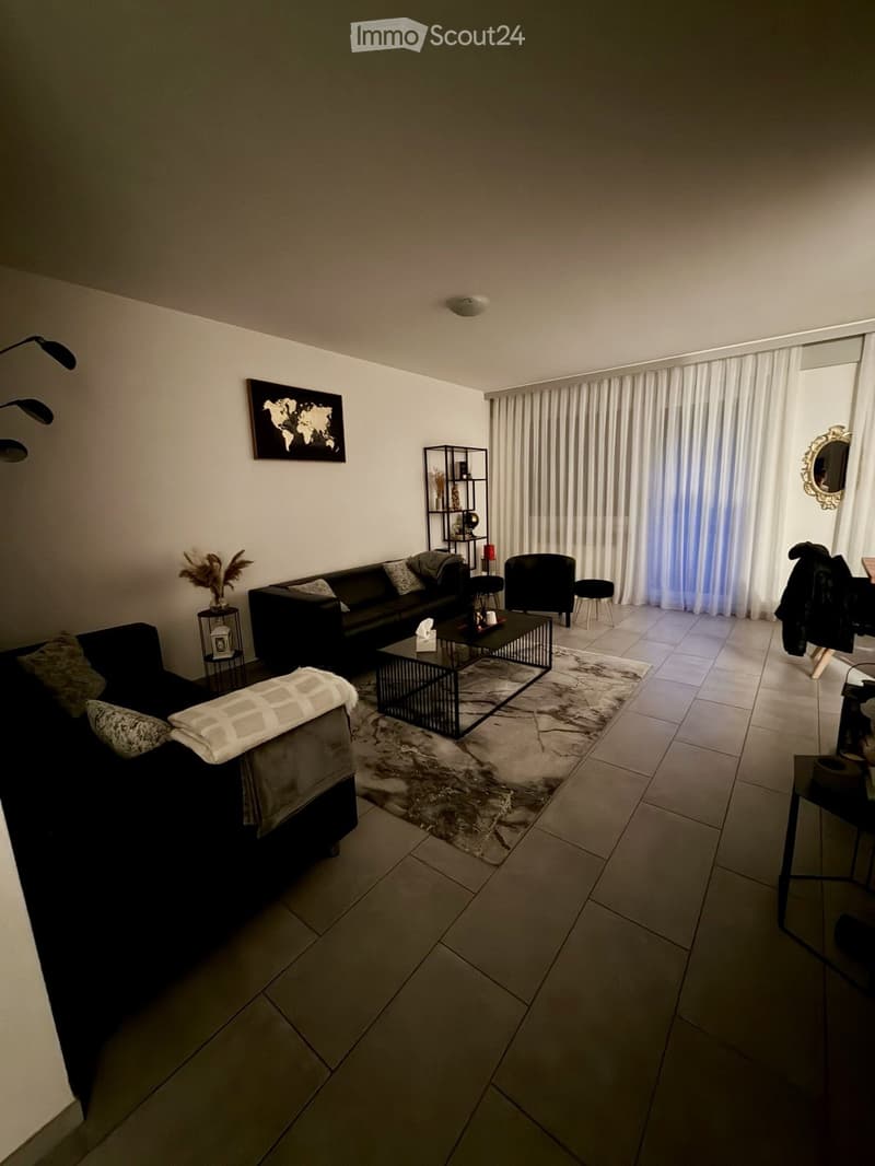 Modern living room with a black sectional sofa, coffee table, chairs, a large window with white curtains, and decorative items including a world map on the wall.