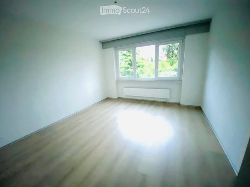 Empty room with white walls, wooden floor, and a single window with white frame and radiator below it.
