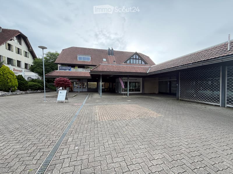 A multi-story building with a tiled roof, a covered entrance area, and a paved courtyard.