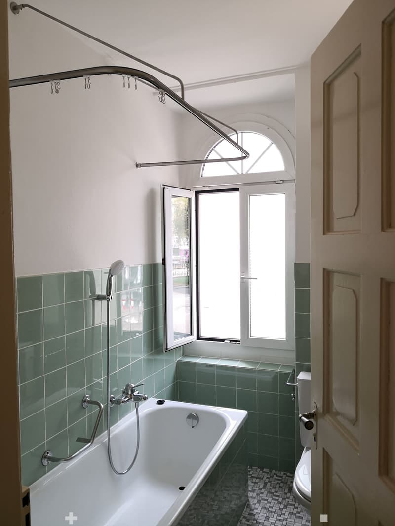 Bathroom with bathtub, overhead shower, window, toilet, tiled floor, and walls