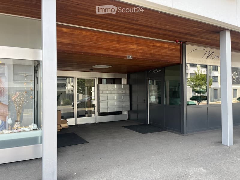 Modern building entrance with a wooden ceiling, glass doors, mailboxes, and a small display area with decorative items.