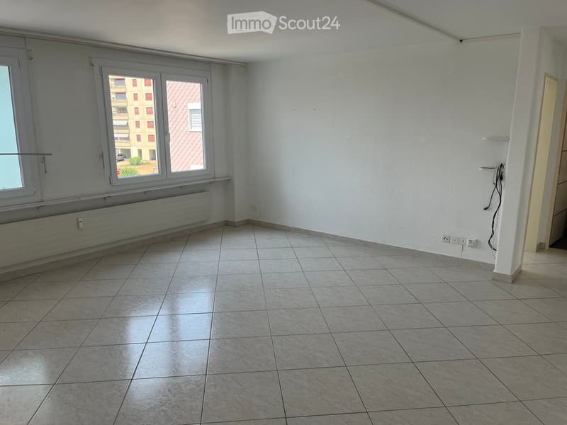 Empty room with tiled floor, white walls, large window with view, radiator, and electrical outlets.