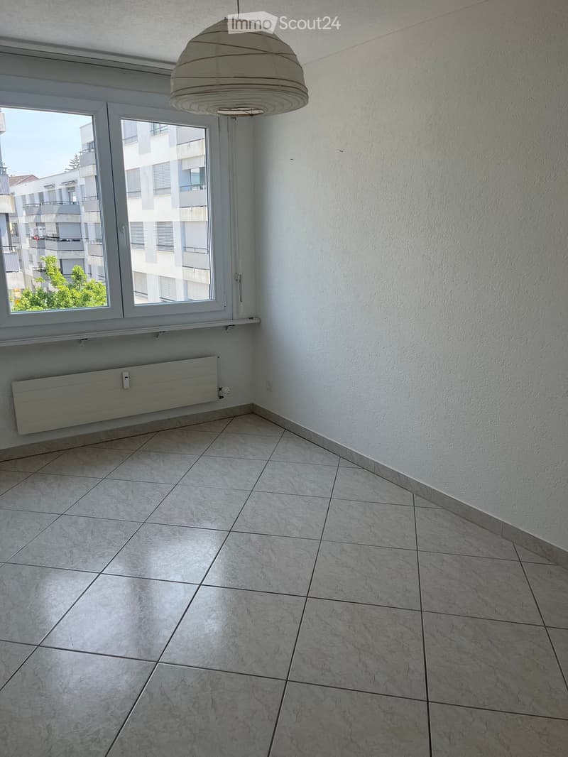 Empty room with tiled floor, white walls, large windows, radiator, and a hanging light fixture.