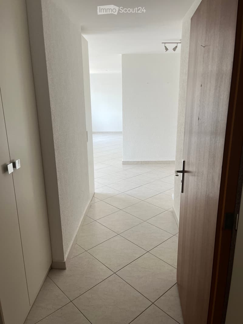 Empty hallway with tiled floor, white walls, and a partially open wooden door leading to another room.