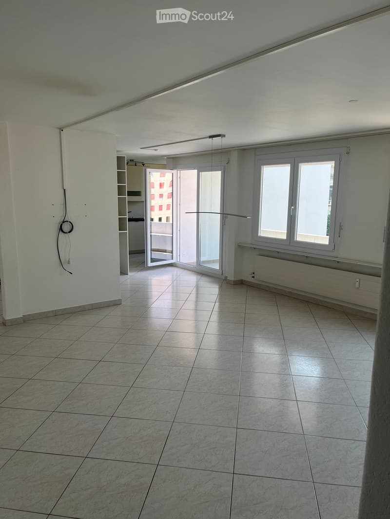 Empty room with tiled floor, white walls, large windows, and an open sliding door leading to a balcony area.