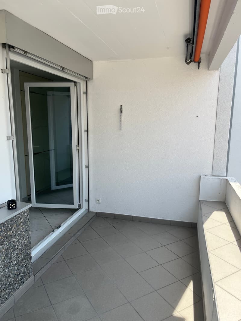 Balcony with tiled floor, white walls, and an open sliding glass door leading to an interior space.