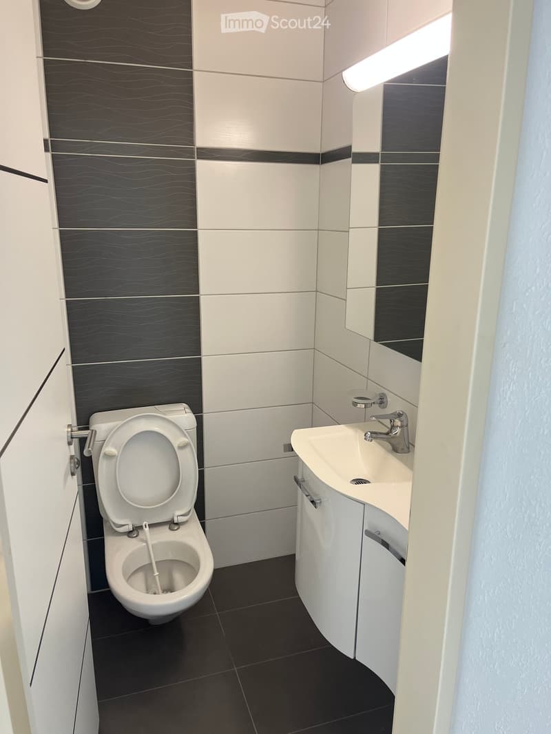 Modern bathroom with white toilet, white sink, chrome faucet, and dark tiled floor.