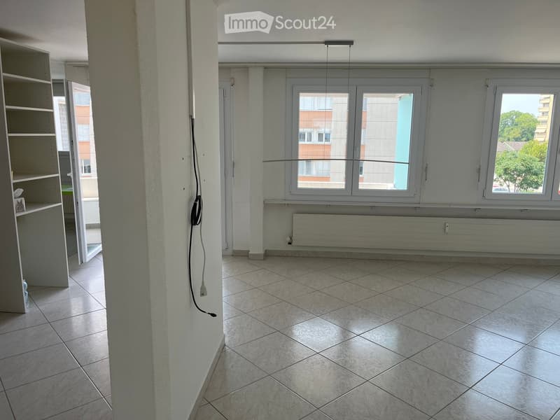 Empty room with tiled floor, white walls, large windows, radiator, and a partially visible shelving unit on the left side.