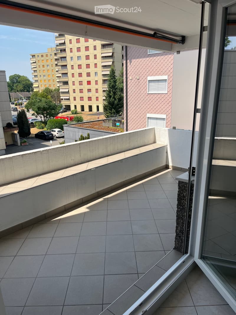 Balcony with tiled floor, low concrete railing, and view of surrounding buildings and parking area.