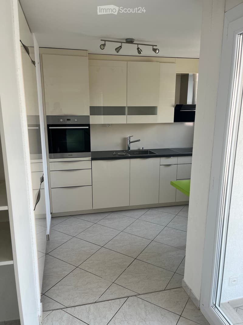 Modern kitchen with white cabinets, stainless steel oven, sink, and faucet, featuring tiled flooring and track lighting.