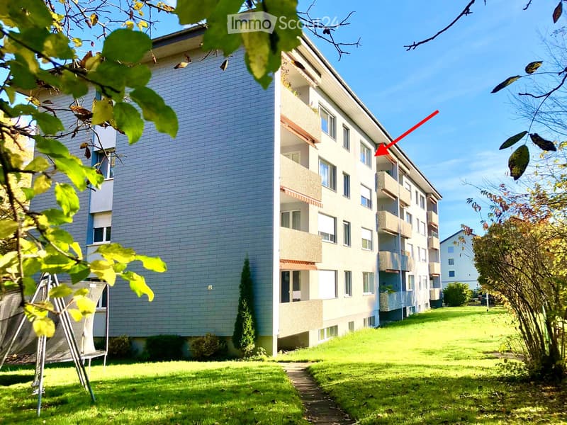 Multi-story residential building with balconies, surrounded by green lawn and trees.