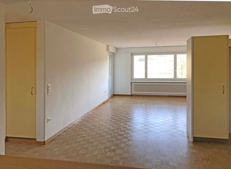 Empty room with wooden flooring, white walls, large windows, and a radiator. No furniture or equipment present.