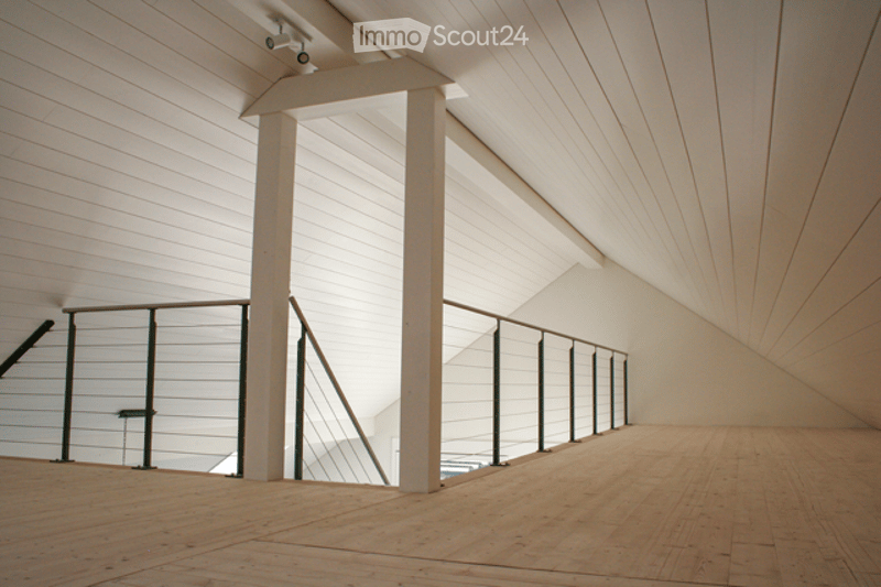 Open, minimalist space with wooden flooring, white paneled walls, and a modern metal railing leading to another level. No furniture or equipment visible.