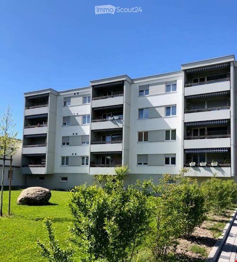 5 story apartment building, white, multiple balconies, garden in front, large rock