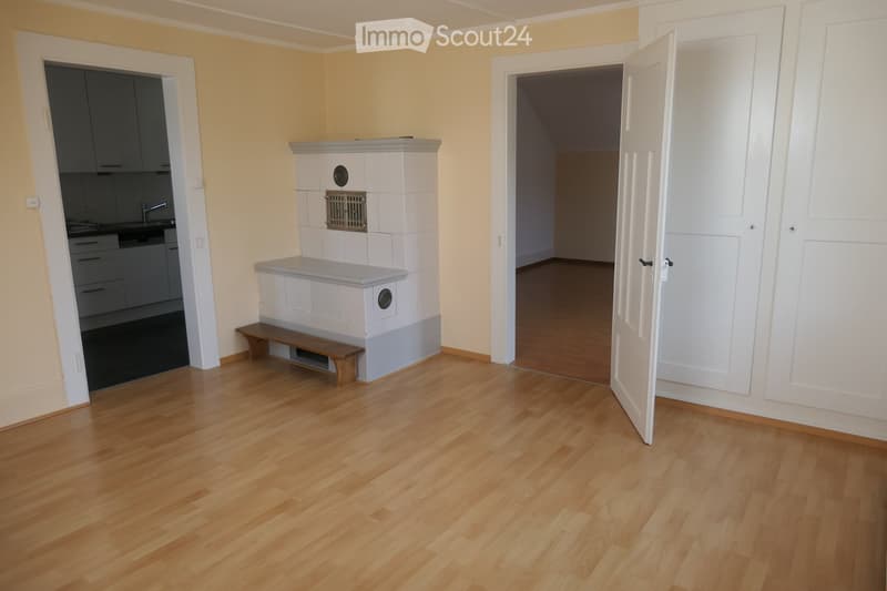 Empty room with light wooden flooring, white walls, and a fireplace with a bench in front of it. The room has two open doors leading to other spaces.