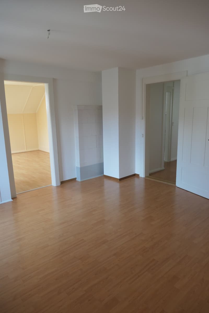 Empty room with wooden flooring, white walls, and two open doorways leading to other spaces.