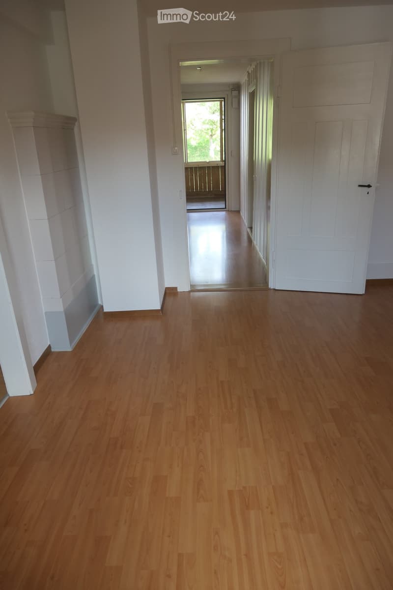 Empty hallway with polished wooden flooring, white walls, and a closed door on the right leading to another room.
