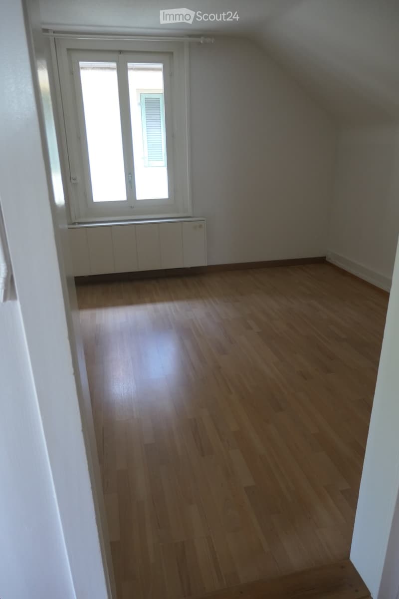 Empty room with wooden flooring, white walls, and a large window with blinds. No furniture or equipment is present.