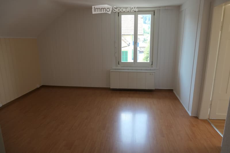 Empty room with wooden flooring, white walls, and a window with white frame. A radiator is placed below the window.