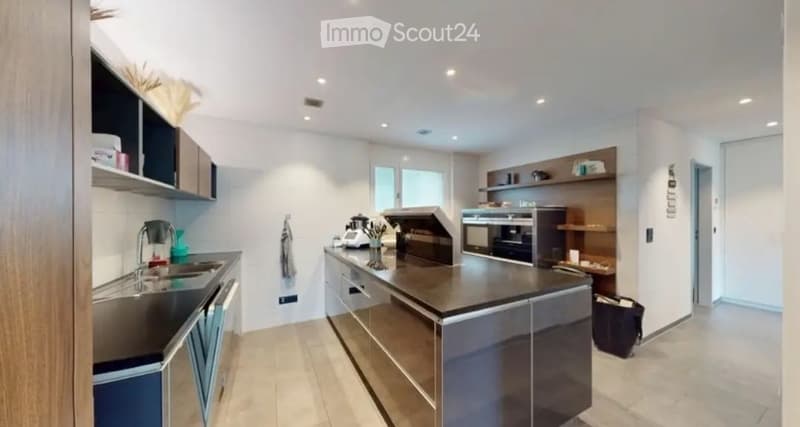 Modern kitchen with stainless steel appliances, dark countertops, and built-in cabinets. Features include a sink, faucet, oven, microwave, coffee maker, and shelves.