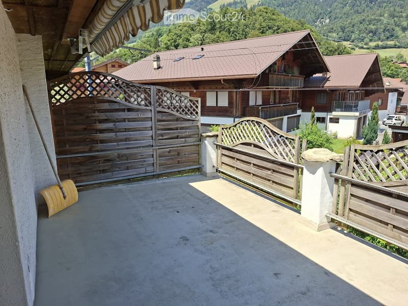 Balcony with wooden fence, concrete floor, and scenic mountain view in the background.