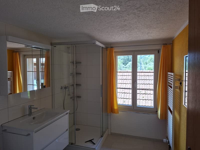 Modern bathroom with a white sink, large mirror, glass-enclosed shower, and yellow curtains on the windows.