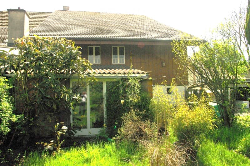 Two-story house with a tiled roof, brick and wooden exterior, multiple windows, and a small covered porch area.