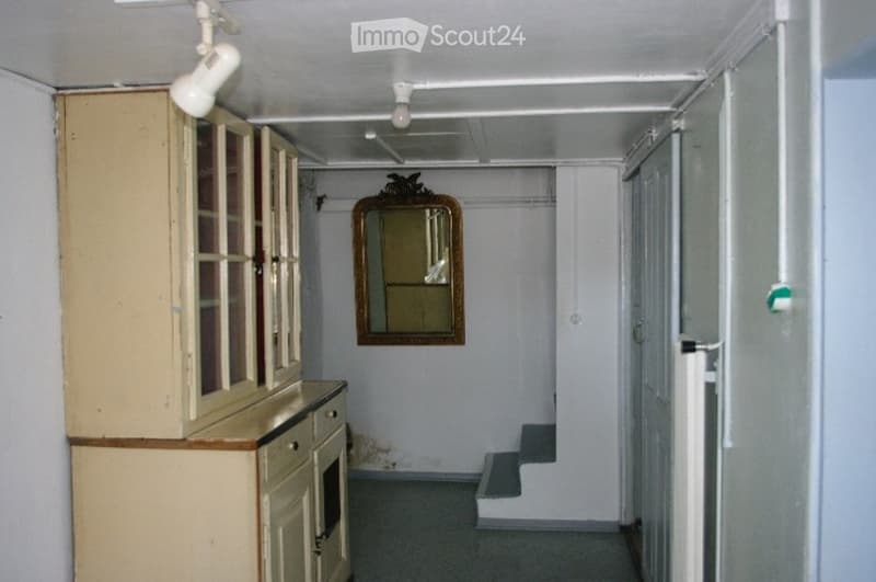 A narrow hallway with a small cabinet on the left, a mirror on the wall, and a staircase leading upwards.