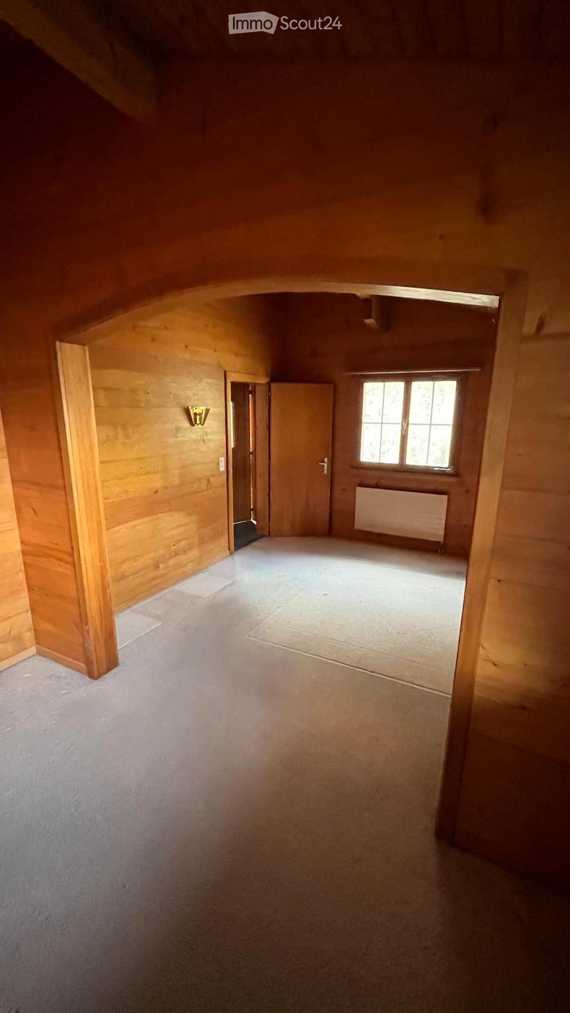 Empty room with wooden walls, carpeted floor, and a window with white frame. No furniture or equipment present.