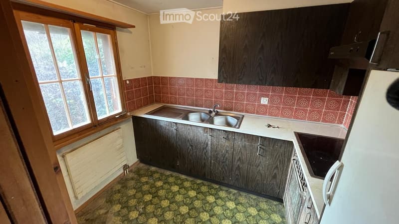Kitchen with dark wooden cabinets, a double sink, and a window with wooden frame. The floor has a patterned tile design, and the walls feature red tiled backsplash.