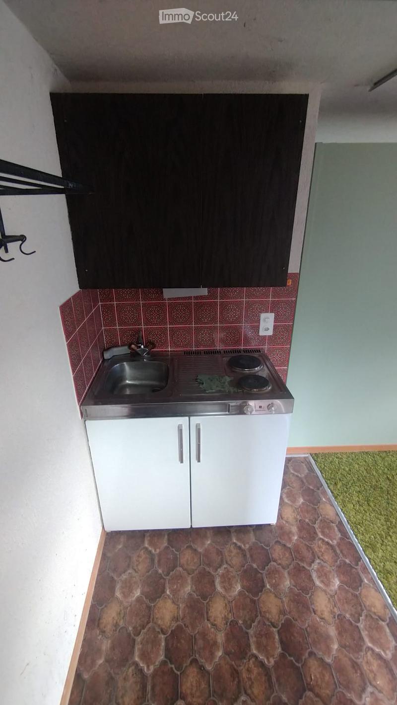 Compact kitchen with white lower cabinets, black upper cabinets, a sink, and a small electric stove. The walls feature red patterned tiles above the counter, and the floor has a patterned tile design.