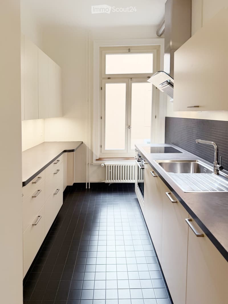 Modern kitchen with white cabinets, black tiled floor, stainless steel sink, and built-in oven.