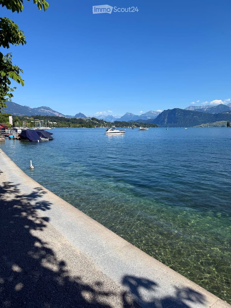 A serene lakeside scene with clear water, boats, and distant mountains under a blue sky.