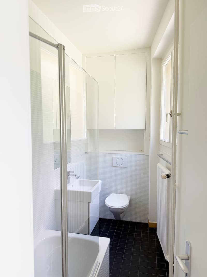 Modern bathroom with white tiles, black floor, sink, toilet, bathtub, and radiator.