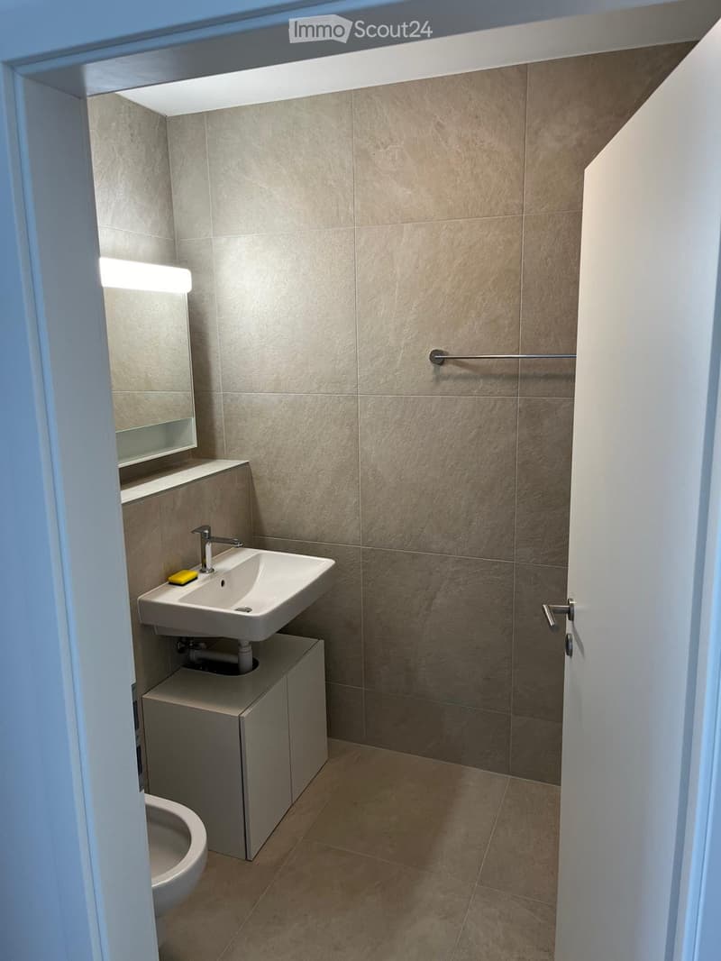 Modern bathroom with beige tiled walls and floor, white sink with chrome faucet, mirrored cabinet, and toilet.