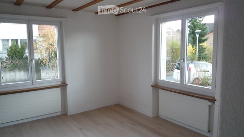Empty room with wooden flooring, white walls, large windows, and radiators beneath the windows.