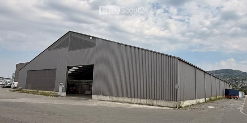 Large industrial building with a grey metal exterior, large garage door open, and visible storage inside.