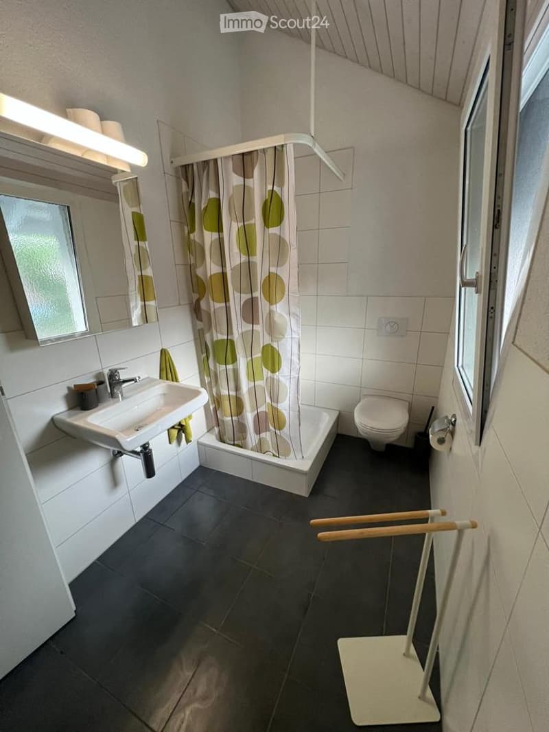 Modern bathroom with white tiles, dark grey floor, sink, bathtub, toilet, mirror, and towel rack.