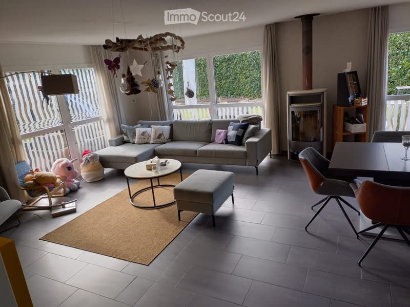 Modern living room with grey sofa, coffee table, ottoman, dining table, chairs, fireplace, and decorative toys.