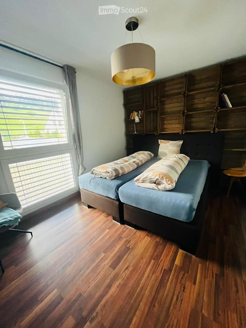 Bright bedroom with two single beds, wooden flooring, built-in shelving, and a hanging pendant light.