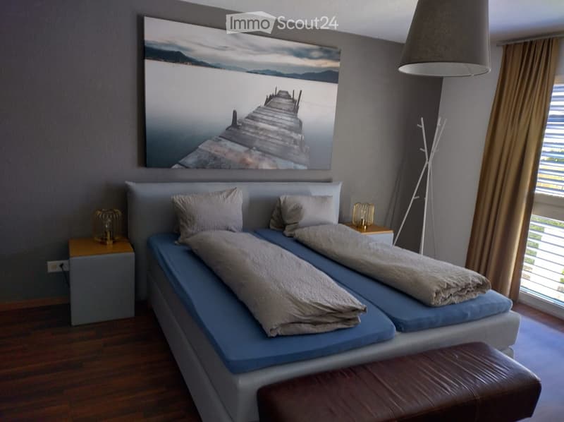 Modern bedroom with a large bed, nightstands, a leather stool, and a large picture frame on the wall.
