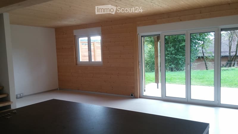 Empty room with wooden walls and ceiling, large sliding glass doors leading to a garden, and a small window on the side wall.