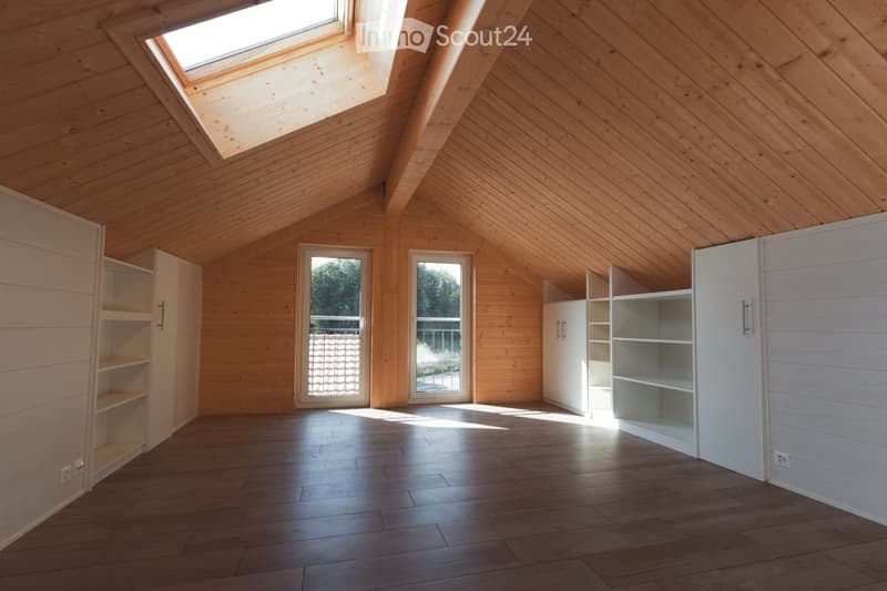 Bright, airy attic room with wooden walls and floors, skylight windows, and built-in white shelving units.