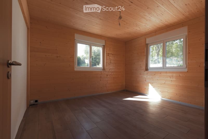 Empty room with wooden walls and floor, two windows, and a door.