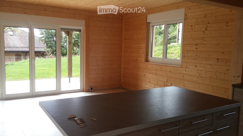 Modern kitchen with light wooden walls, large sliding glass doors, and a dark countertop with keys placed on it.