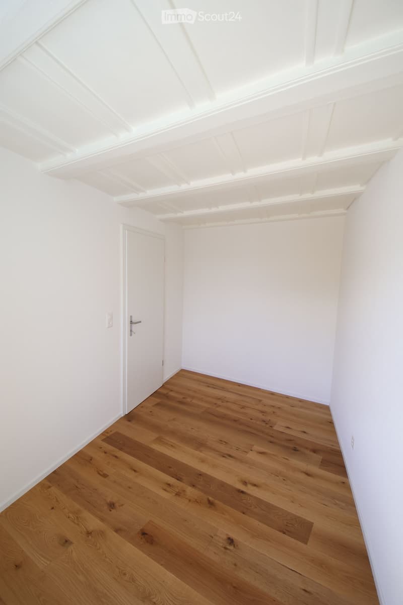 Empty room with white walls, wooden floor, and a white door.