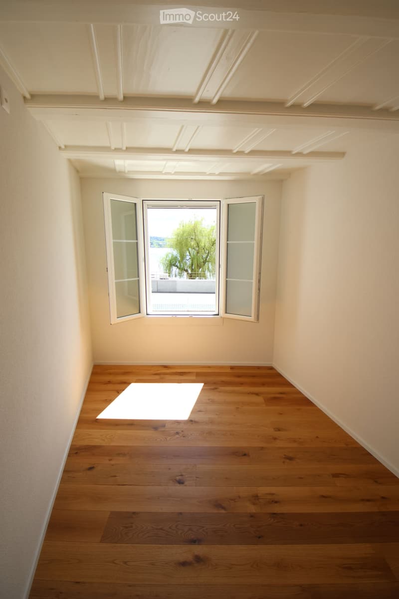 Empty room with wooden flooring, white walls, and large windows with open shutters, allowing natural light to fill the space.