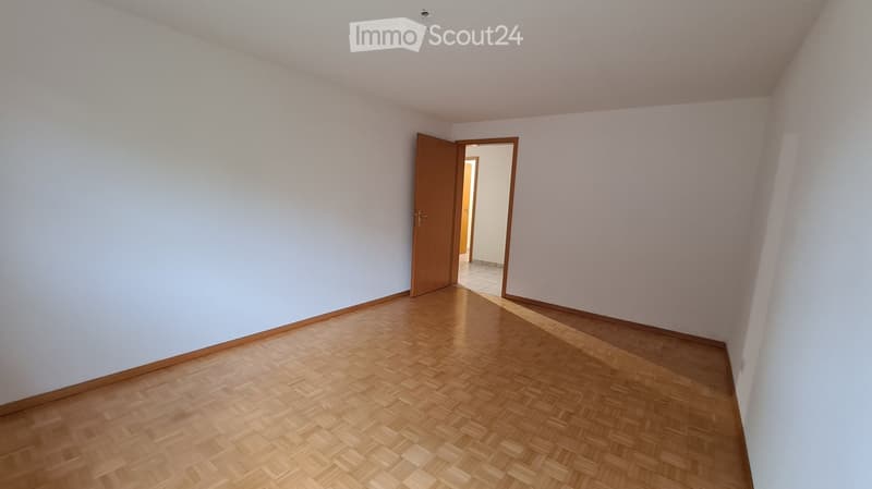 Empty room with light-colored walls and wooden flooring, featuring an open doorway leading to another room.