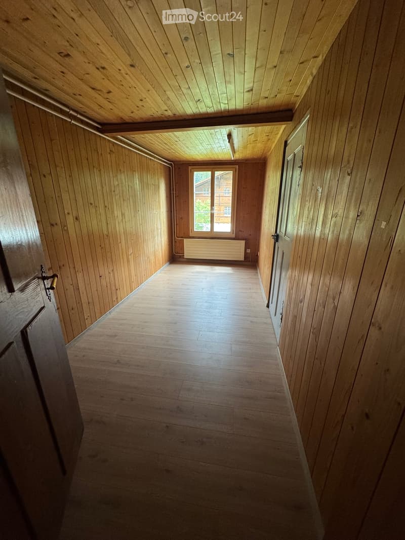 Empty wooden hallway with slanted wooden ceiling, wooden walls, and a window at the end.