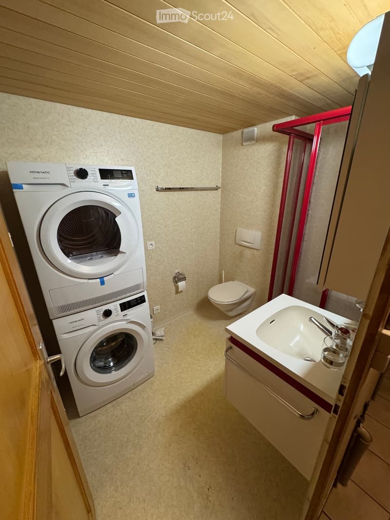 Compact bathroom with a sink, toilet, and stacked washing machine/dryer unit.